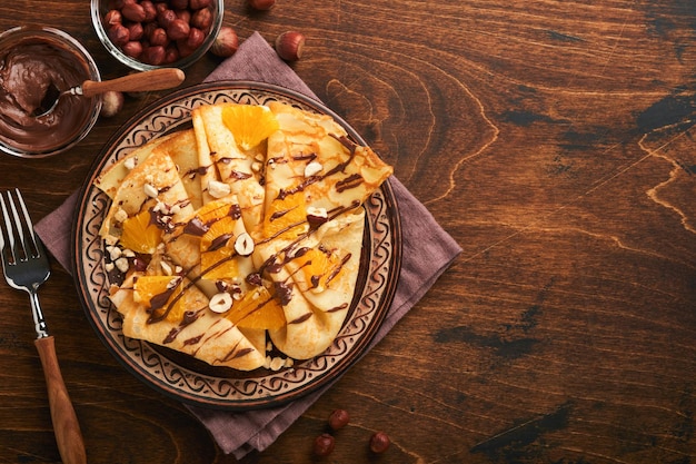 Crêpes suzette aux oranges et au chocolat Crêpes fines aux noisettes à tartiner au chocolat et tranches d'orange fruits en assiette pour le petit-déjeuner sur fond de table rustique en bois foncé ancien Espace de copie Vue de dessus