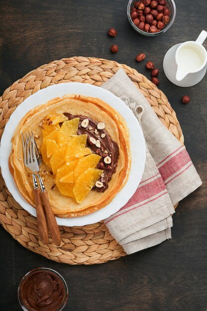 Crêpes suzette aux oranges Crêpes fines aux noisettes à tartiner au chocolat et tranches d'orange fruits dans une assiette blanche pour le petit-déjeuner sur fond de table rustique en bois foncé ancien Espace de copie Vue de dessus