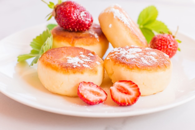 Crêpes de syrniki, de caillé ou de fromage cottage à la fraise, sucre en poudre sur une table blanche.