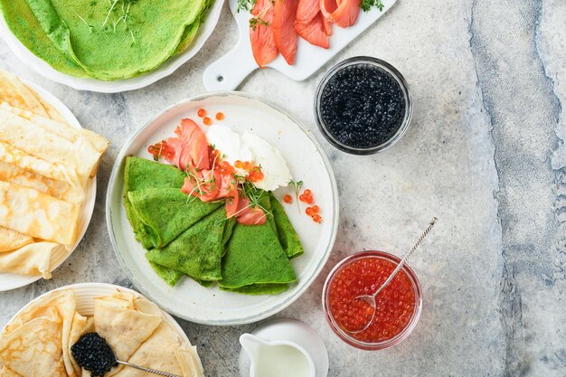 Crêpes vertes et blanches assorties Crêpes fines aux épinards verts et crêpes blanches avec sauce au caviar rouge et noir sur fond de table en béton gris petit-déjeuner Journée nationale des crêpes ou mardi gras