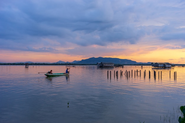 Crépuscule du ciel au coucher du soleil dans le lac avec vue sur la montagne, ciel nuageux et petit pêcheur