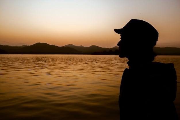 Crépuscule Femme Lac Silhouette sur fond de montagnes Orange Sky. Femme libre appréciant la liberté se sentant heureuse au coucher du soleil. Femme relaxante sereine dans un pur bonheur.