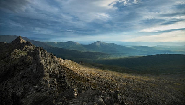 La crête escarpée de la montagne sous un ciel spectaculaire jette des ombres sur le vaste paysage serein qui s'étend au loin.