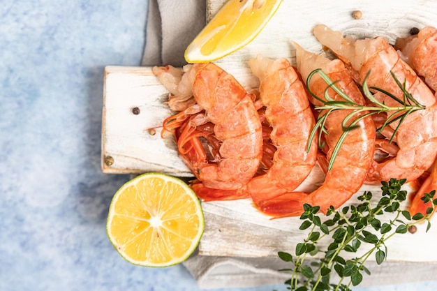 Crevettes argentines crues sur une planche à découper en bois blanc avec des herbes de citron vert et du poivre