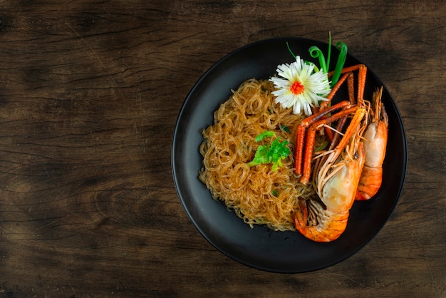 Crevettes au four avec vermicelles de nouilles en verre dans une assiette noire Cuisine chinoise de style asiatique décorer Corainder légumes thaïlandais et poireau sculpté vue de dessus d'oignon