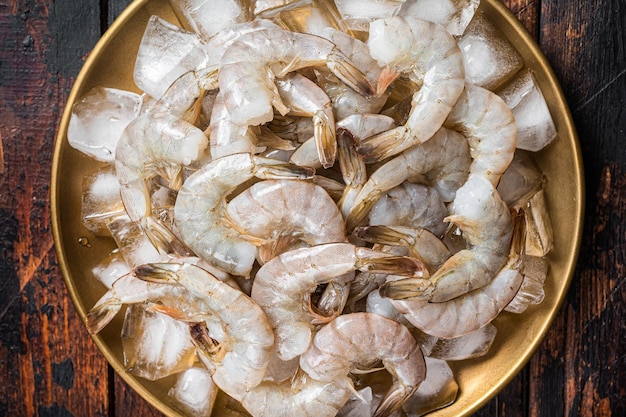 Crevettes blanches tigrées crues fraîches décortiquées avec la queue sur la glace Fond en bois Vue de dessus