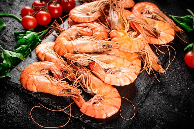 Crevettes bouillies sur une planche en pierre avec tomates et persil