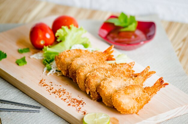 Crevettes Butterfly Ebi furai servies avec tomate et laitue sur une planche à découper en bois