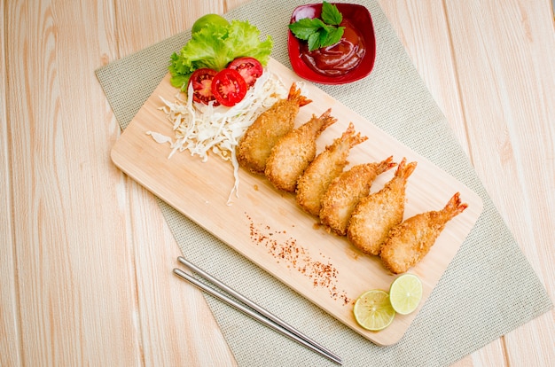 Crevettes Butterfly Ebi furai servies avec tomate et laitue sur une planche à découper en bois