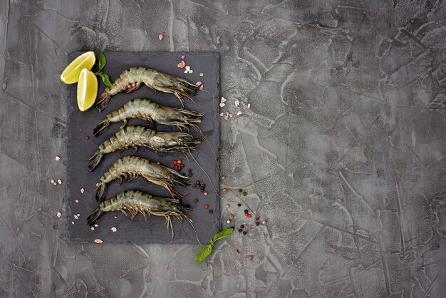 Crevettes crevettes crues fraîches au citron vert et épices sur une planche en pierre. Les fruits de mer sains sont une source de protéines. Mise à plat. Copiez l'espace.