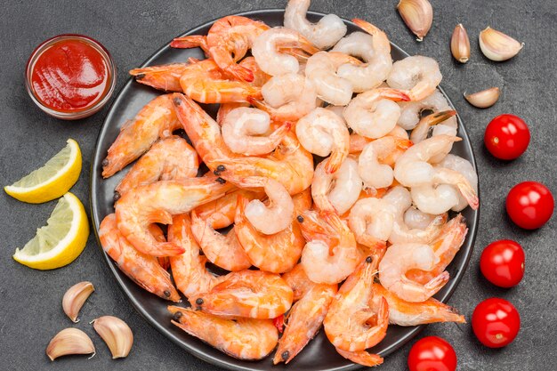 Crevettes et crevettes tigrées dans un bol noir. Tomates, gousses d'ail citron sur table.