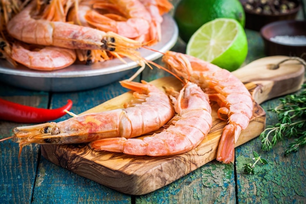 Crevettes crues fraîches sur une planche à découper en bois avec sel poivre citron vert sur une table rustique