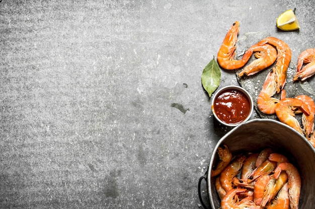 Crevettes dans une vieille casserole avec sauce et épices. Sur un fond de pierre.