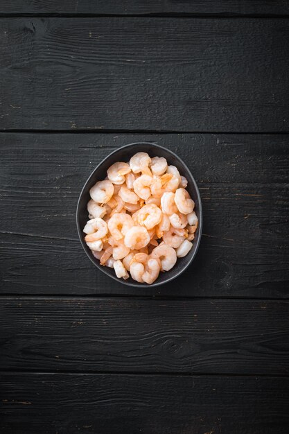 Crevettes décortiquées bouillies, dans un bol, sur une table en bois noir, vue de dessus à plat