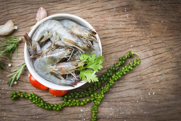 Crevettes fraîches sur bol blanc et fond en bois avec des ingrédients herbes et épices pour la cuisson des fruits de mer - crevettes crues crevettes