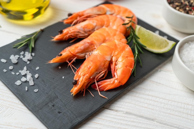 Photo des crevettes fraîches avec du citron vert et du romarin sur une table en bois blanc