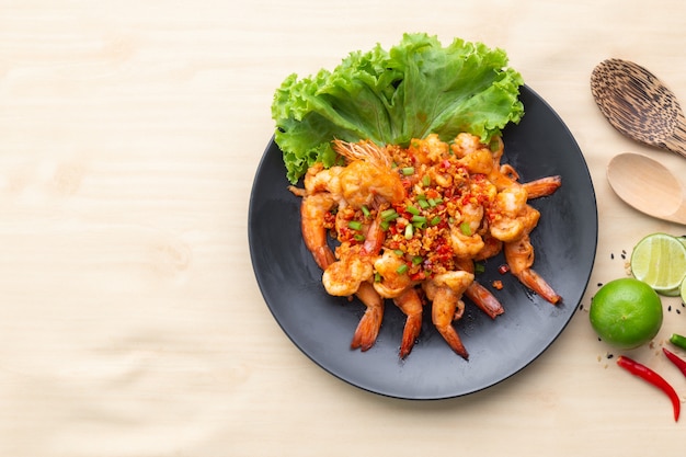 Crevettes frites avec du poivre et du sel dans une assiette noire sur une table en bois, l'un des plats célèbres en Thaïlande.