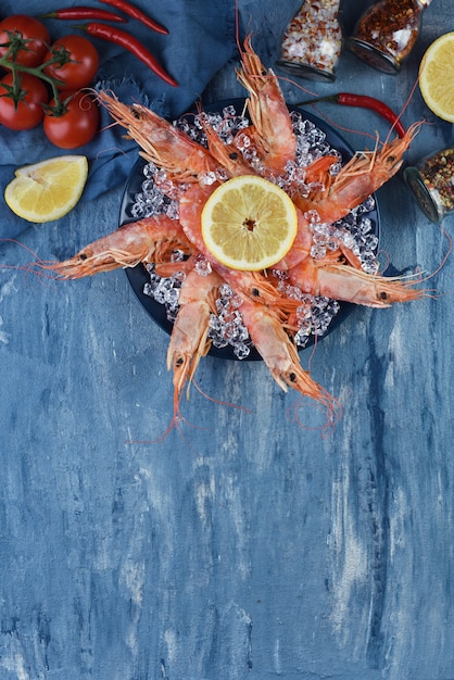 Crevettes Géantes Sur Une Plaque Avec De La Glace Et Du Citron Sur Fond Bleu Avec Copie Espace. Menu Ou Recette De Fruits De Mer. Vue De Dessus Des Crevettes Aux Légumes.