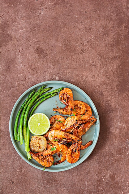 Crevettes grillées crevettes tigrées aux épices avec des asperges et une tranche de citron vert sur une assiette sur ab