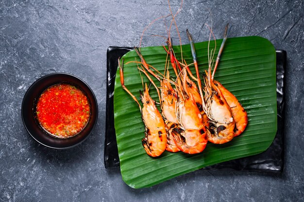 Crevettes grillées sur plaque noire avec sauce épicée sur table.