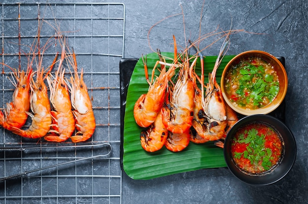 Crevettes grillées sur plaque noire avec sauce épicée sur table.