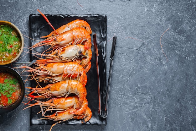 Crevettes grillées sur plaque noire avec sauce épicée sur table.