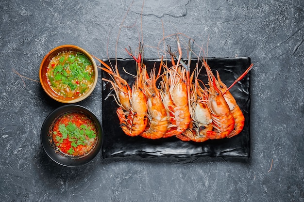 Crevettes grillées sur plaque noire avec sauce épicée sur table.