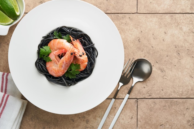 Photo crevettes de pâtes spaghetti noires sur plaque noire sur fond de table en béton clair pâtes à l'encre de calmar aux crevettes pâtes aux fruits de mer vue de dessus sur table en pierre noire plat de cuisine traditionnelle méditerranéenne