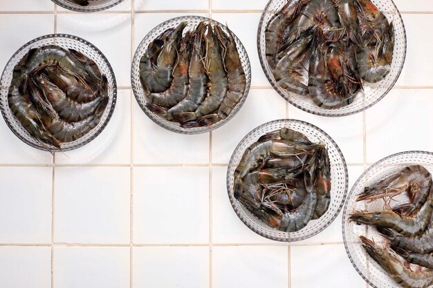 Crevettes tigrées noires fraîches sur une plaque émaillée prête à être préparée sur une table en marbre noir rustique, avec garniture au citron, vue d'en haut, espace de copie