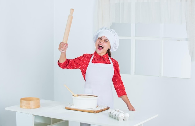 Criant adolescente cuisson pâte enfant en uniforme de chef culinaire et cuisine