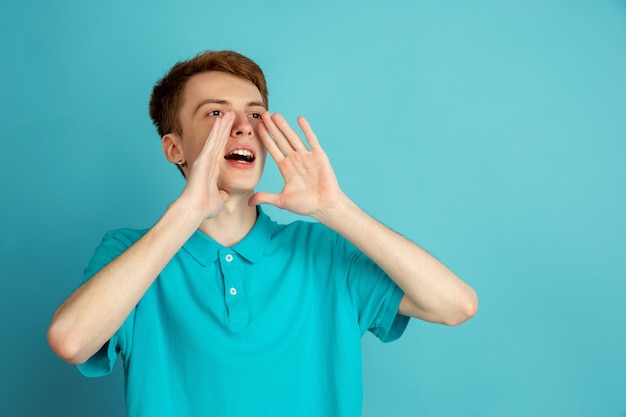 Crier, appeler. Portrait moderne du jeune homme caucasien isolé sur mur bleu, monochrome. Beau modèle masculin.