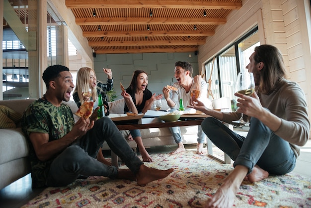 Crier cinq amis assis dans la maison et manger de la pizza