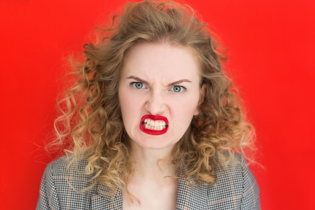 Photo crier, haine, rage. femme émotionnelle est en colère sur fond de studio rouge. visage émotionnel, jeune, bannière web. émotions faciales expressives