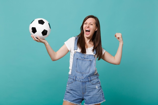 Crier une jeune femme folle de football qui encourage l'équipe favorite de soutien avec un ballon de football faisant le geste du vainqueur isolé sur fond de mur bleu turquoise. Émotions des gens, concept de loisirs sportifs en famille.