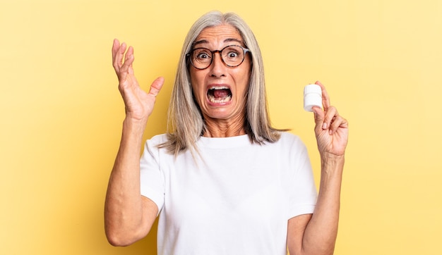 Crier avec les mains en l'air, se sentir furieux, frustré, stressé et bouleversé et tenir une bouteille de pilules