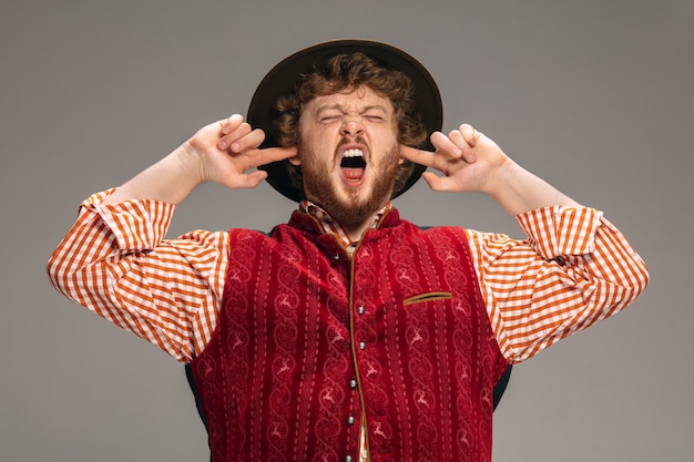 Crier les oreilles fermées. Homme habillé en costume traditionnel autrichien ou bavarois gesticulant isolé sur fond gris studio. Espace de copie. La célébration, l'oktoberfest, le festival, le concept de traditions.