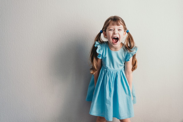 Photo crier petite fille en robe bleue sur mur neutre