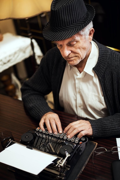 Écrivain senior rétro avec chapeau, écrivant sur une machine à écrire obsolète.