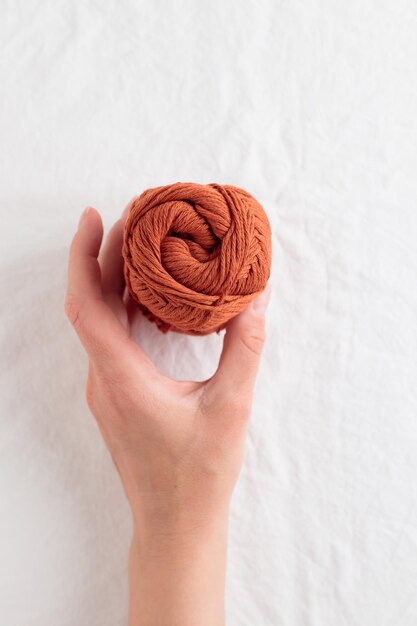 Crochet et pelote de fil de coton couleur ocre dans une main sur un tableau blanc