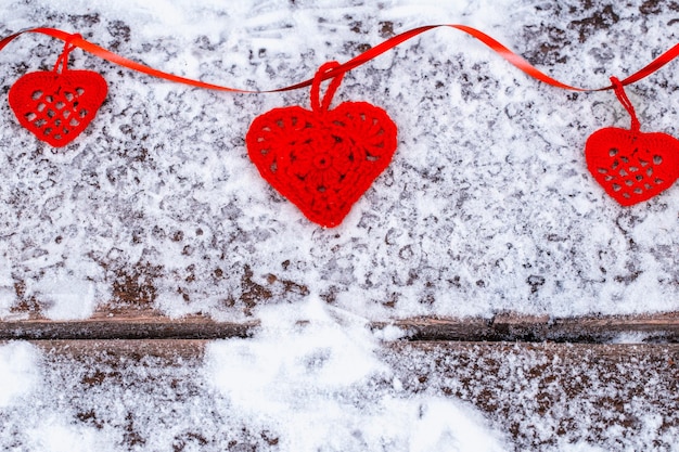 Crocheter Des Coeurs Rouges Avec Un Ruban Sur Une Planche Rugueuse Recouverte De Neige. Fond De Saint Valentin