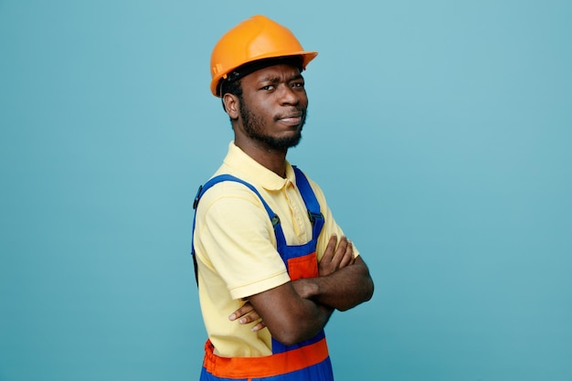 Croisement confiant mains jeune constructeur afro-américain en uniforme isolé sur fond bleu