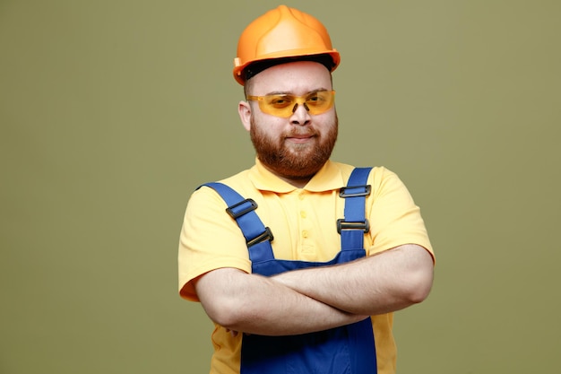 Croisement confiant mains jeune constructeur homme en uniforme isolé sur fond vert