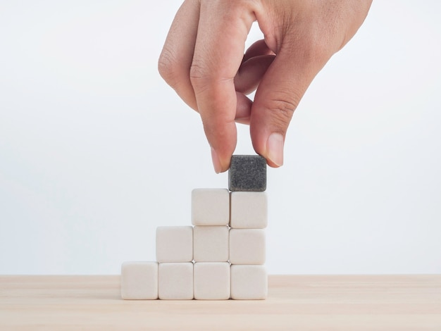 Croissance de l'entreprise, concept de processus de construction d'avantages. Mettez à la main le dernier bloc de cubes de dés noirs de différence sur des blocs de cubes de dés blancs s'empilant comme escalier sur une table en bois sur fond blanc.