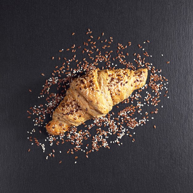 Photo croissant aux graines de sésame et de lin sur fond noir en pierre, vue de dessus