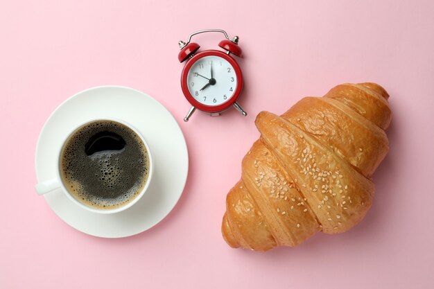 Croissant, café et réveil sur rose