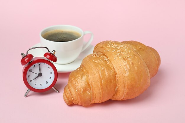 Croissant, café et réveil sur rose