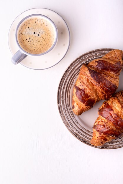 Croissant chaud et une tasse de café sur une table en bois blanc. Matin nature morte. Vue de dessus avec espace pour le texte.