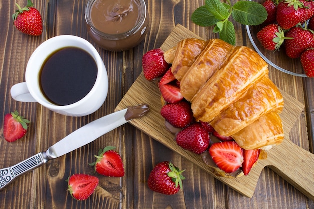 Croissant avec crème au chocolat et fraise sur la planche à découper en bois.Vue de dessus.