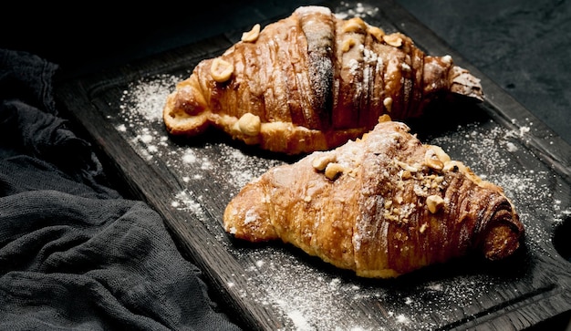 Croissant cuit au four sur une planche de bois et saupoudré de sucre en poudre tableau noir Pâtisseries appétissantes pour le petit déjeuner