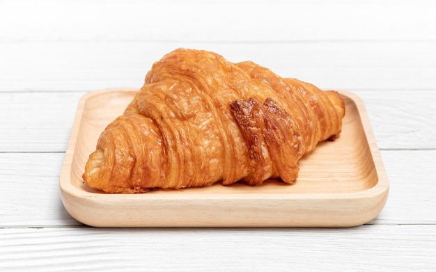 Croissant la délicieuse boulangerie dans une assiette en bois sur fond de bois blanc vintage